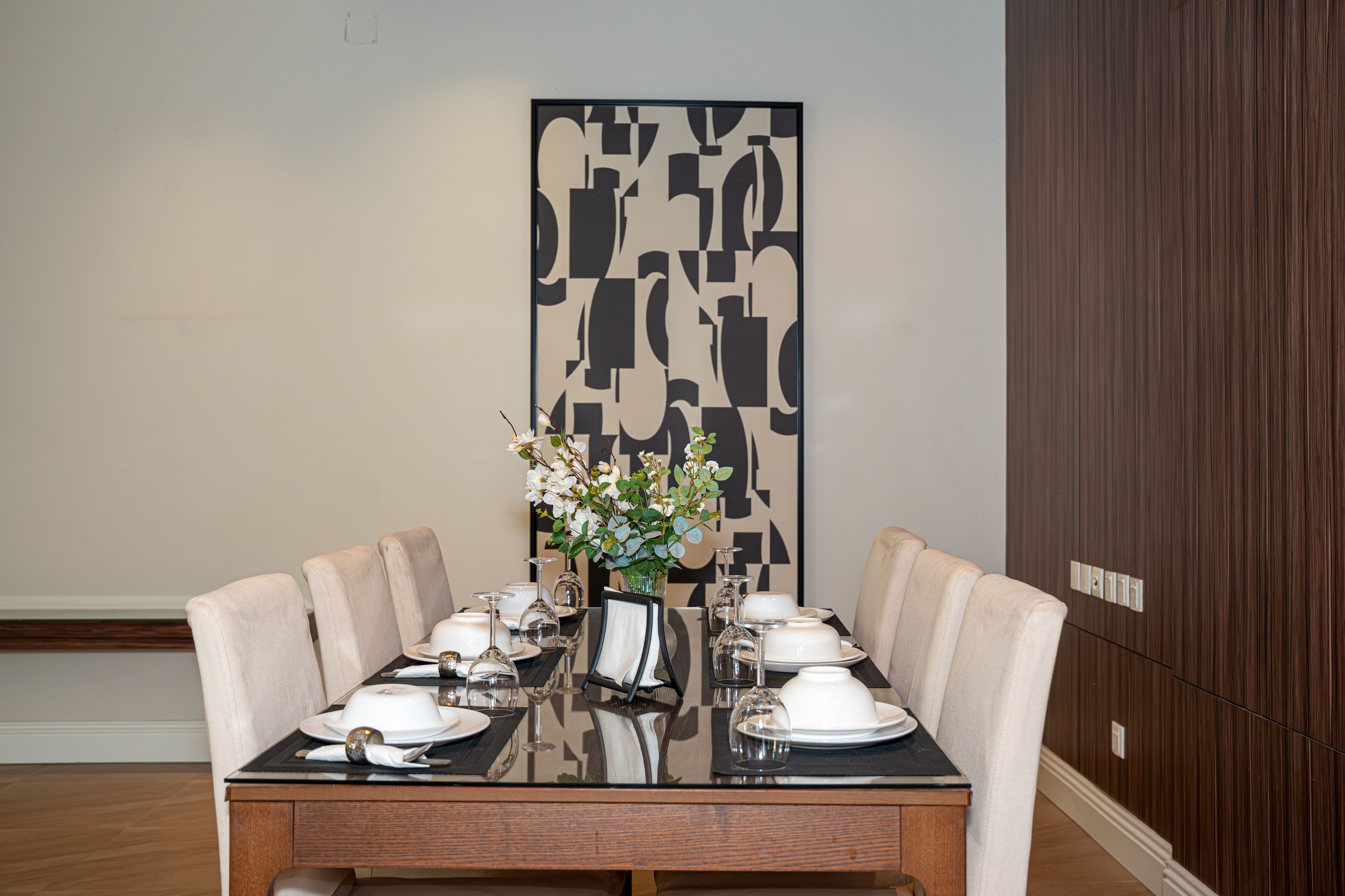 A dining table set with white plates, glasses, and a vase of flowers.