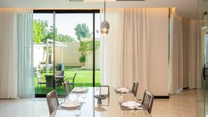 Un espace repas moderne avec une table en verre, des chaises et une vue sur un jardin, grâce à de grandes fenêtres.