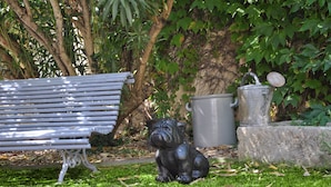 A park bench, a metal trash can, and a statue of a bulldog.