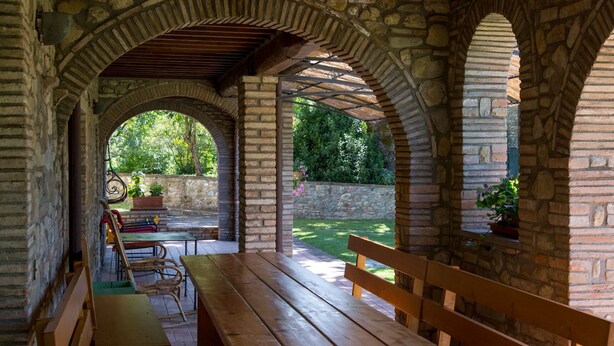 An outdoor patio with stone arches, wooden benches, and a table.