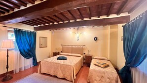 A bedroom with two beds, a wooden ceiling, a nightstand, a lamp, and a window with curtains.