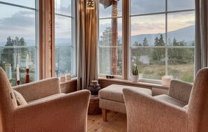 Une pièce chaleureuse, avec des fauteuils en osier, une petite table et une vue sur les montagnes grâce à de grandes fenêtres.