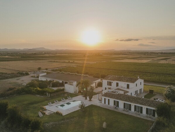 A large house with a swimming pool and multiple rooms, surrounded by fields and a sunset in the background. - Vino Resort Son Amaret (Manacor)