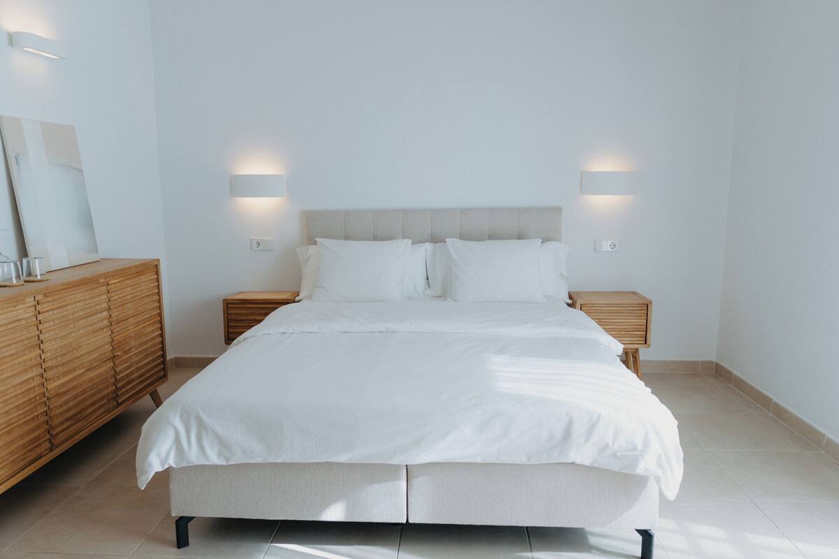 A neatly arranged bedroom with a large bed, two bedside tables, a wooden dresser, and wall-mounted lamps.