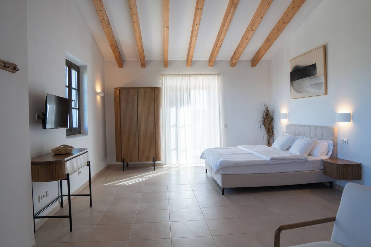 A bedroom with a bed, bedside tables, a TV, and a window with curtains.