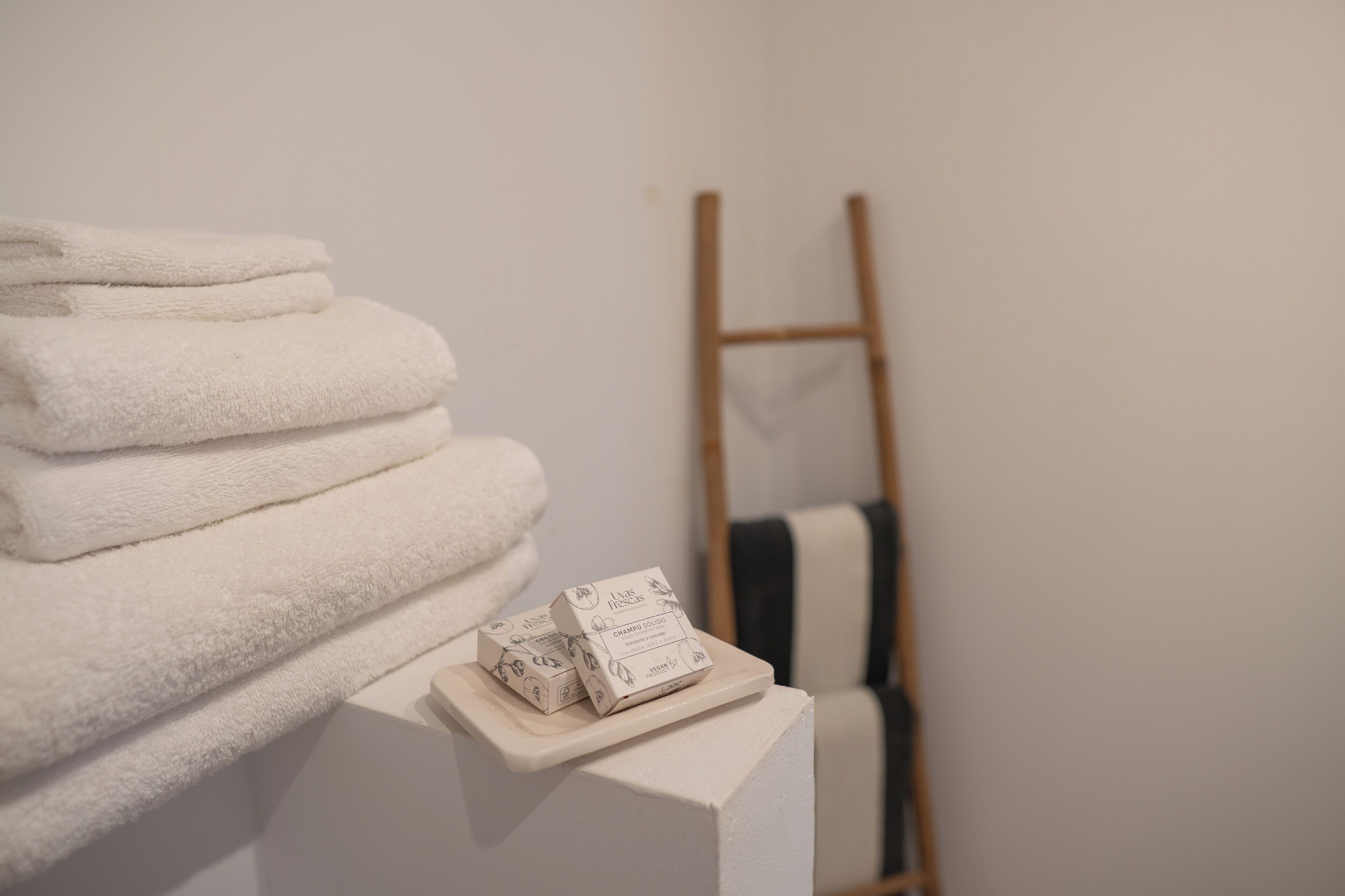 A stack of white towels on a white pedestal with a wooden ladder in the background.