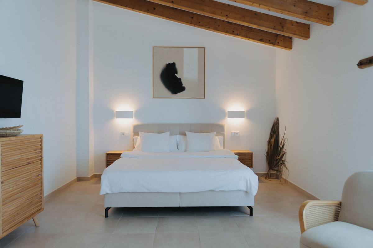 A modern bedroom with a large bed, wooden headboard, bedside lamps, and a mounted artwork.