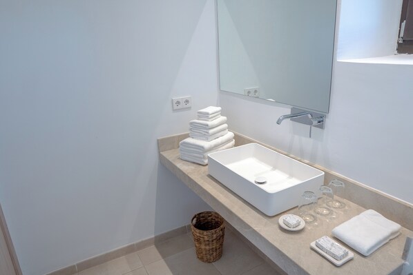 A modern bathroom with a large white sink, a mirror, and neatly stacked towels. - Vino Resort Son Amaret (Manacor)