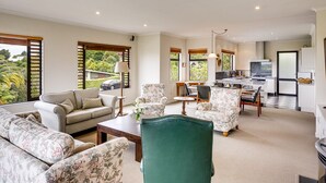 A spacious living room with a sofa, chairs, and a dining area. - Busby Hill Villa - Havelock North Holiday Home (Havelock North)