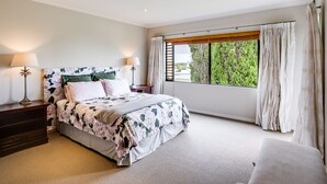 A bedroom with a large bed, a nightstand, a lamp, and a window with curtains. - Busby Hill Villa - Havelock North Holiday Home (Havelock North)