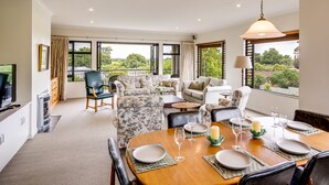 A spacious living room with a dining area, large windows, and a view of the outdoors. - Busby Hill Villa - Havelock North Holiday Home (Havelock North)