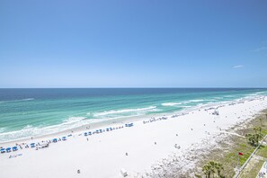 A beach with white sand, clear blue water, and a few umbrellas.