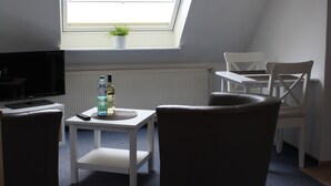Quarto pequeno e moderno com claraboia, televisão, uma mesa com duas garrafas e duas cadeiras.