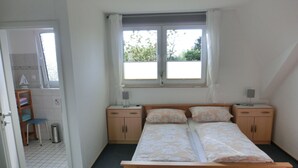 Quarto com uma cama, duas mesas de cabeceira, uma janela e uma porta que dá para o banheiro.