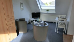 A compact room with a sloped ceiling, a television, a small table with bottles, a white chair, and a wooden wardrobe. - Vacation home in a quiet location - Neuwerk 3 (Cuxhaven)