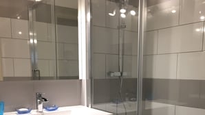 Moderni kylpyhuone, jossa on lasinen suihkuseinä, valkoinen pesuallas, jonka yläpuolella on peili, sekä tumman sävyinen allaskaappi laatikoilla.