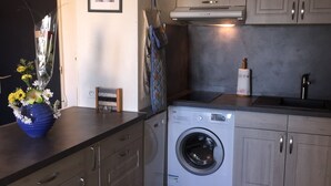 Kompakti keittiö, jossa on sisäänrakennettu pesukone ja kuivausrumpu, puiset kaapit ja tumma työtaso.