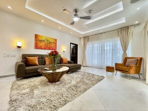 A modern living room with a sofa, a coffee table, and a chair. There is a painting on the wall and a door in the background. - Amazing Twin Terrace 5 bedrooms 5 baths with Car & Driver Rental Option (Trasacco Valley)