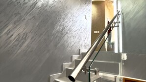 A modern staircase with glass railings and a metal handrail, leading to a room with a wooden door and a textured wall.