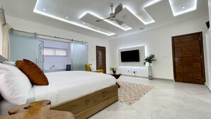 A modern bedroom with a bed, a ceiling fan, recessed lighting, a TV, and a wooden door.
