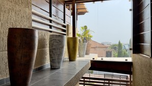 A modern interior with large vases on a shelf, a wooden wall, and a view of buildings and greenery outside.