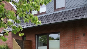 A brick house with a sliding glass door, a small porch with a chair, and a garden with a stone planter.