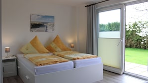 A bedroom with a bed, two bedside lamps, a nightstand, a painting on the wall, and a sliding glass door to a balcony.