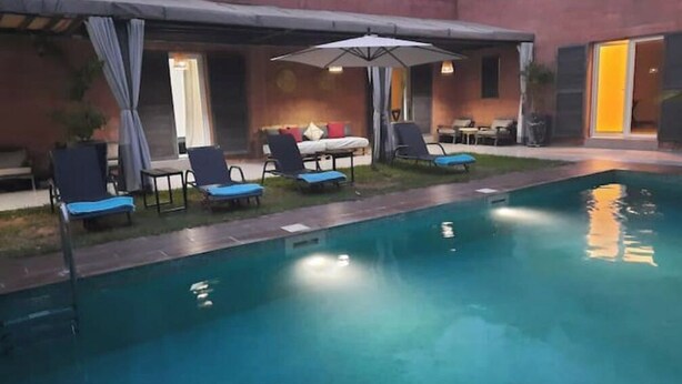 A swimming pool with lounge chairs and umbrellas, surrounded by a building with a covered patio area. - Villa Cactus, 5 Chambres, Piscine Chaufée (Marrakech)