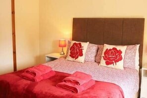 A bed with red linens, a headboard, and two pillows with a red rose design.