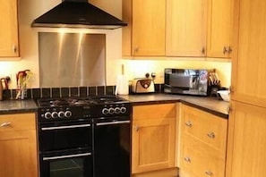 A kitchen with wooden cabinets, a stainless steel range hood, a double oven, and a microwave.