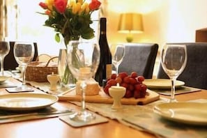 A dining table set with wine glasses, a bottle, a vase with flowers, and a cheese board.