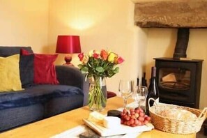 A cozy living room with a sofa, a table with a vase of flowers, a basket, and a wood-burning stove.