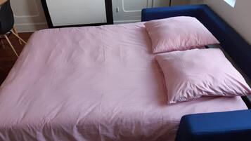 Ein Bett mit einer rosa Bettdecke und Kissen, einem blauen Kopfteil und einem Fenster mit Tageslicht.