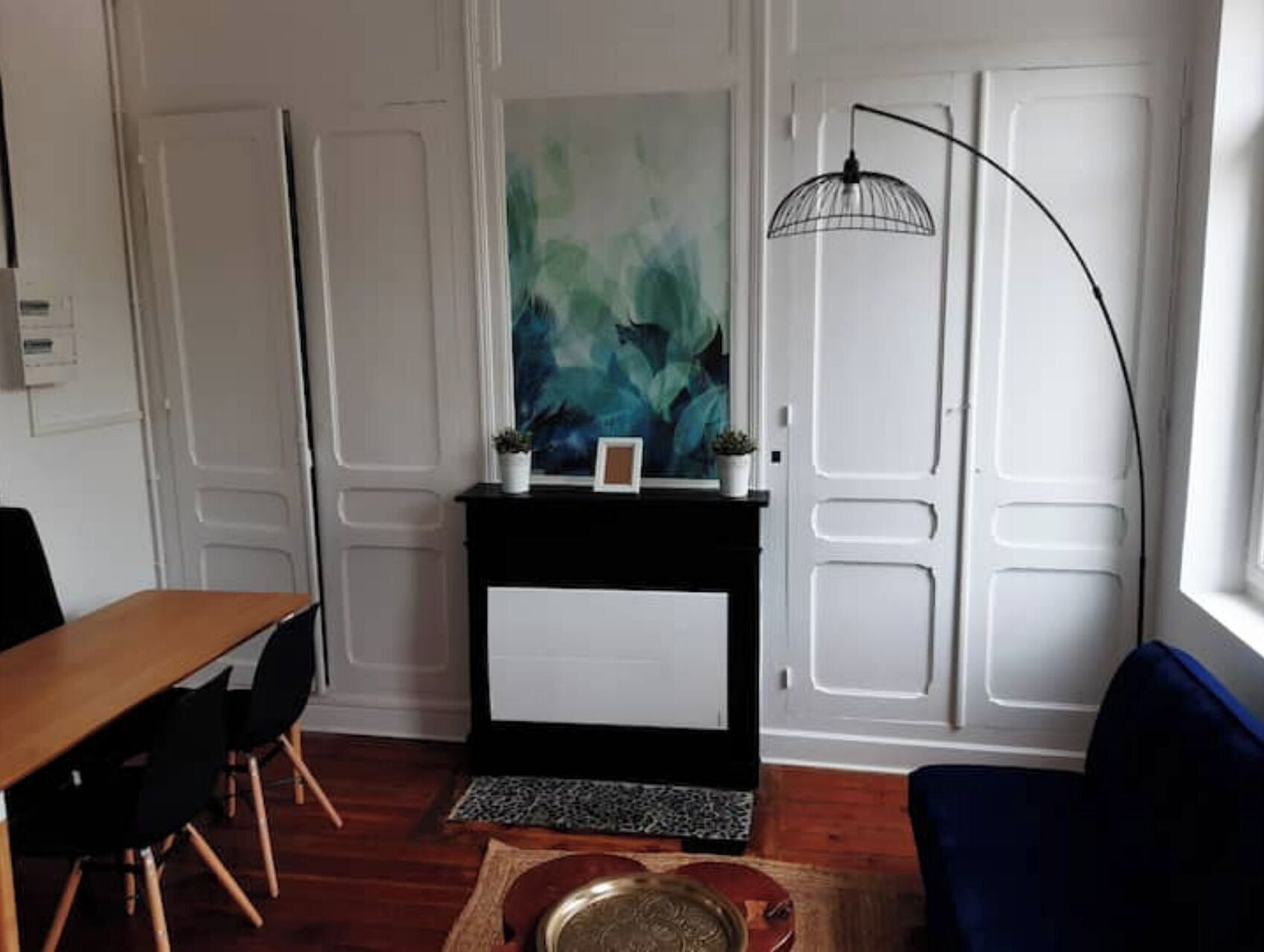 En stue med pejs, et billede, et spisebord med stole og en blå lænestol.