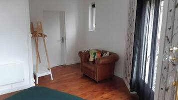 A room with a wooden floor, a brown leather sofa, a green ottoman, a white door, and a window with curtains.