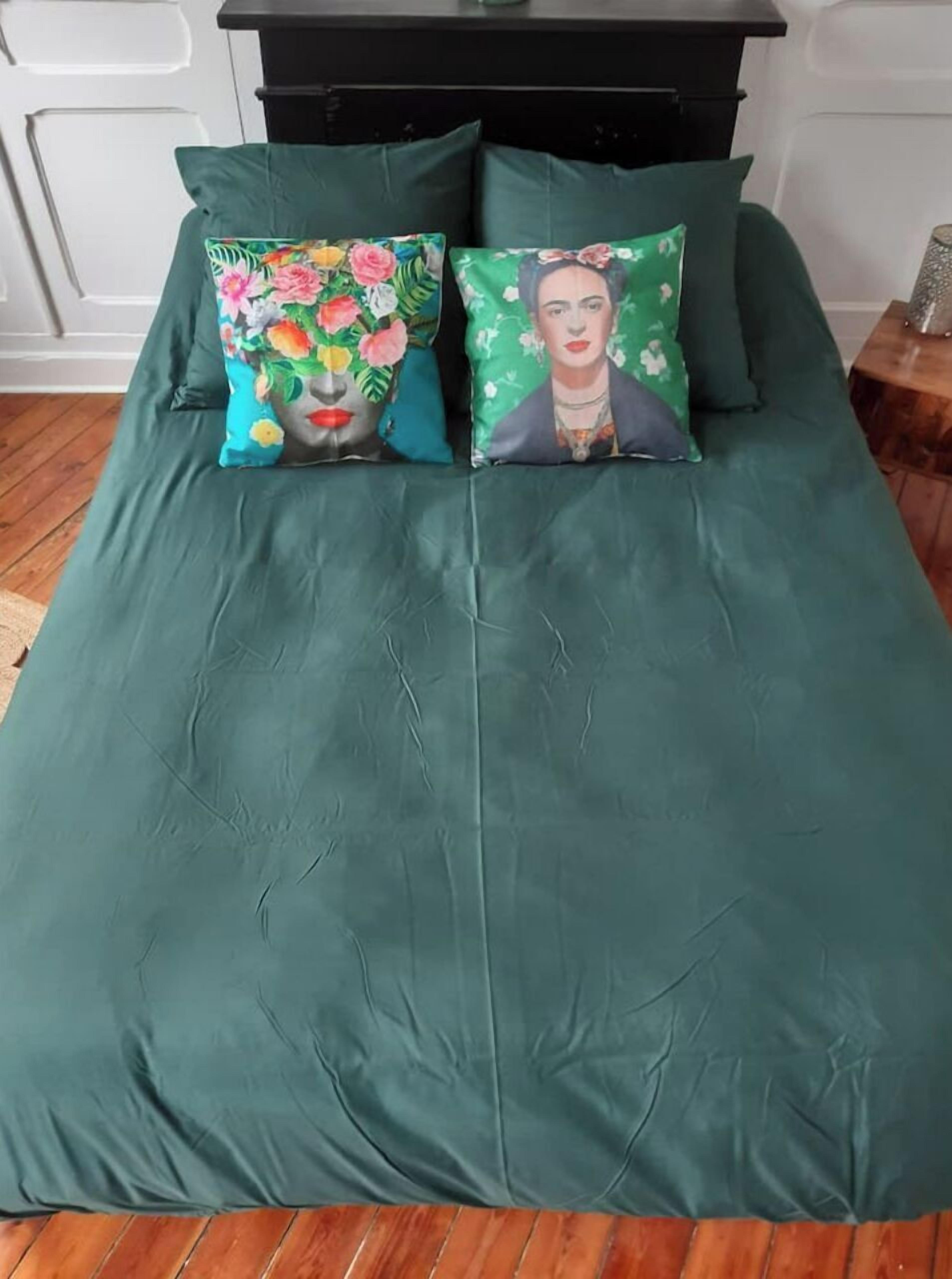 A bed with a green bedspread and two decorative pillows.