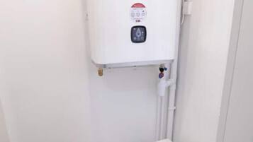 Une petite salle de bain blanche, avec des toilettes, une cuvette blanche et des tuyaux apparents.