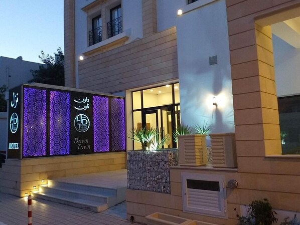 A hotel entrance with illuminated signage, a stone facade, and a welcoming outdoor area with steps and potted plants. - Downtown Tunis Hotel (Tunis)