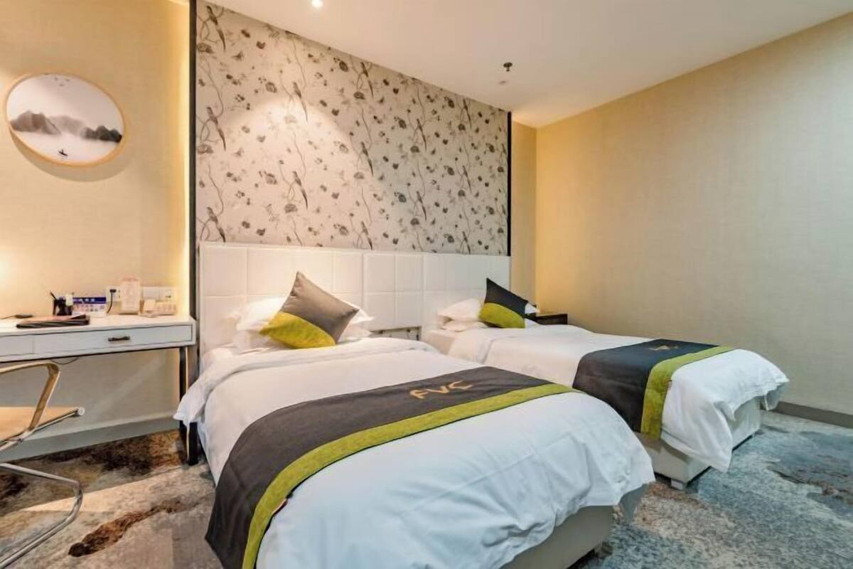 A hotel room with two beds, a desk, and a wall with a floral pattern.