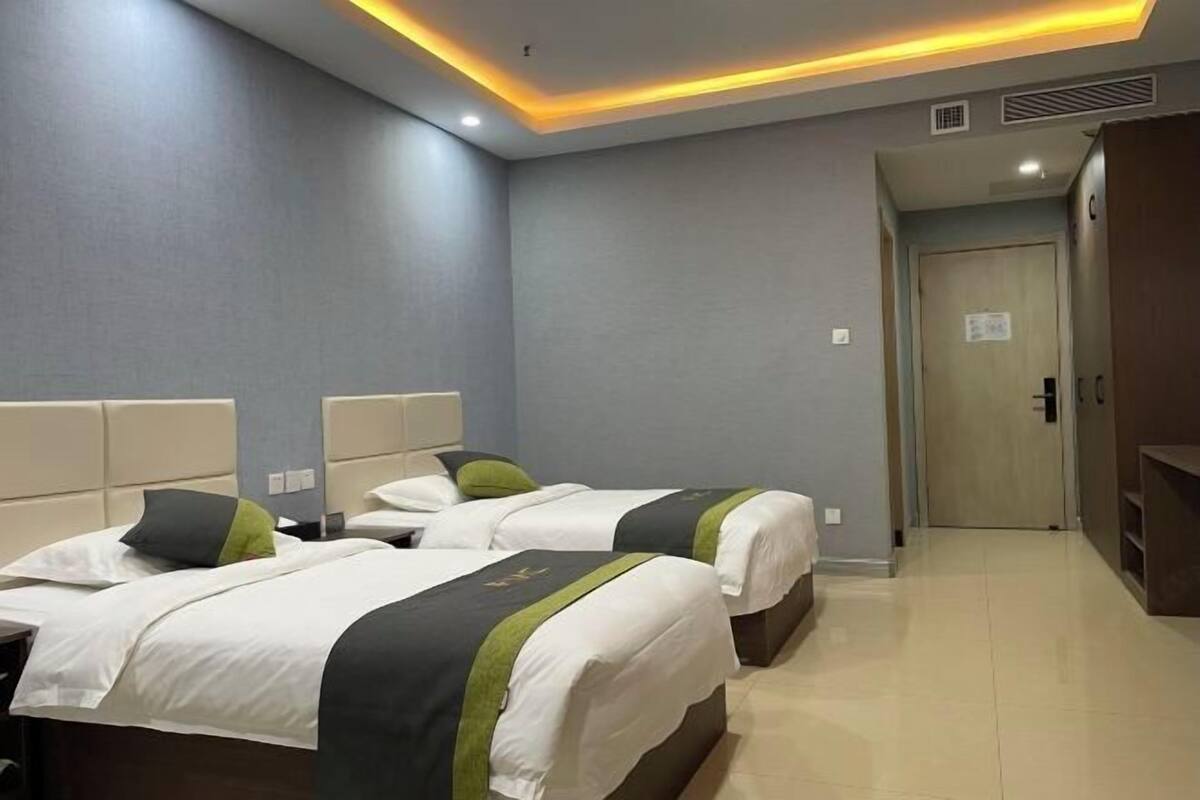 A hotel room with two beds, a wooden wardrobe, and a door leading to another room.