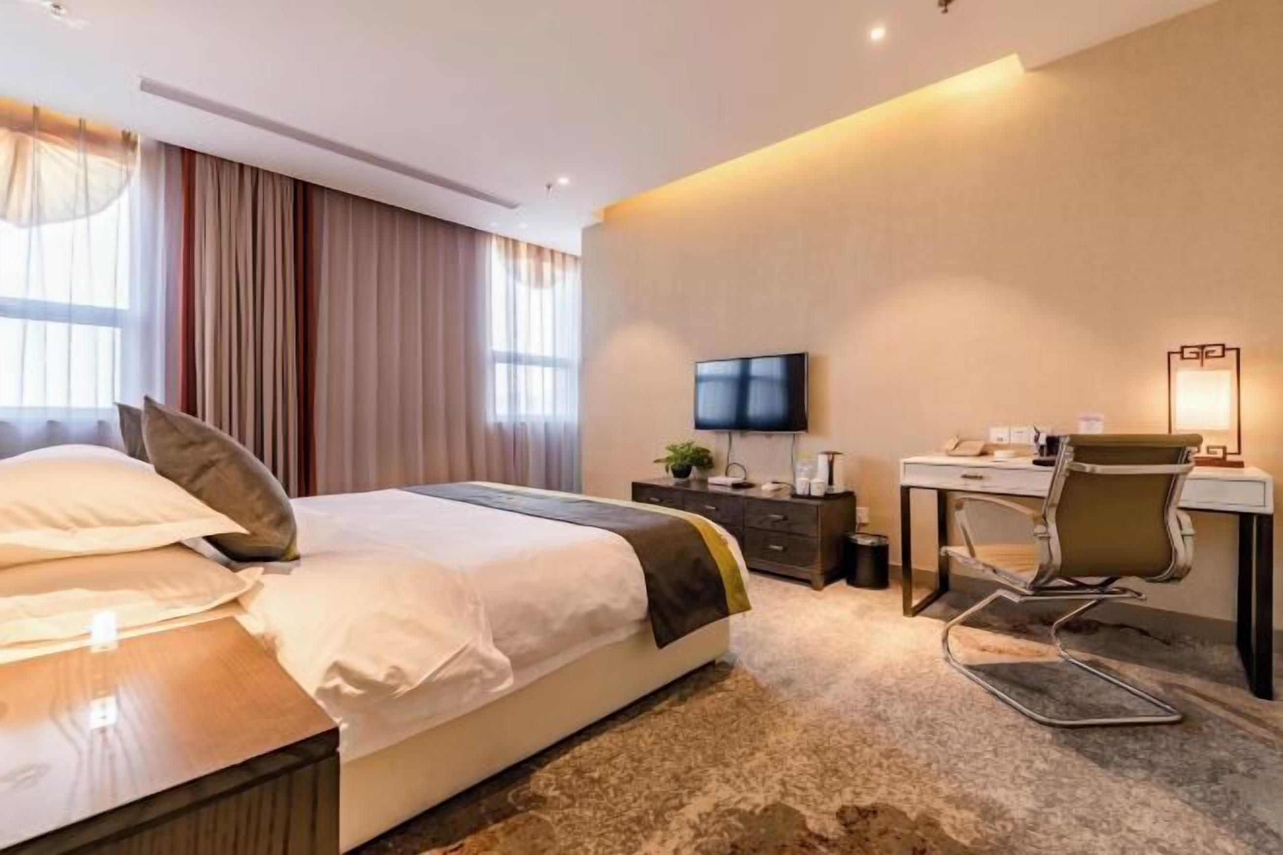 Una habitación de hotel con cama, escritorio, silla, televisor y lámpara.