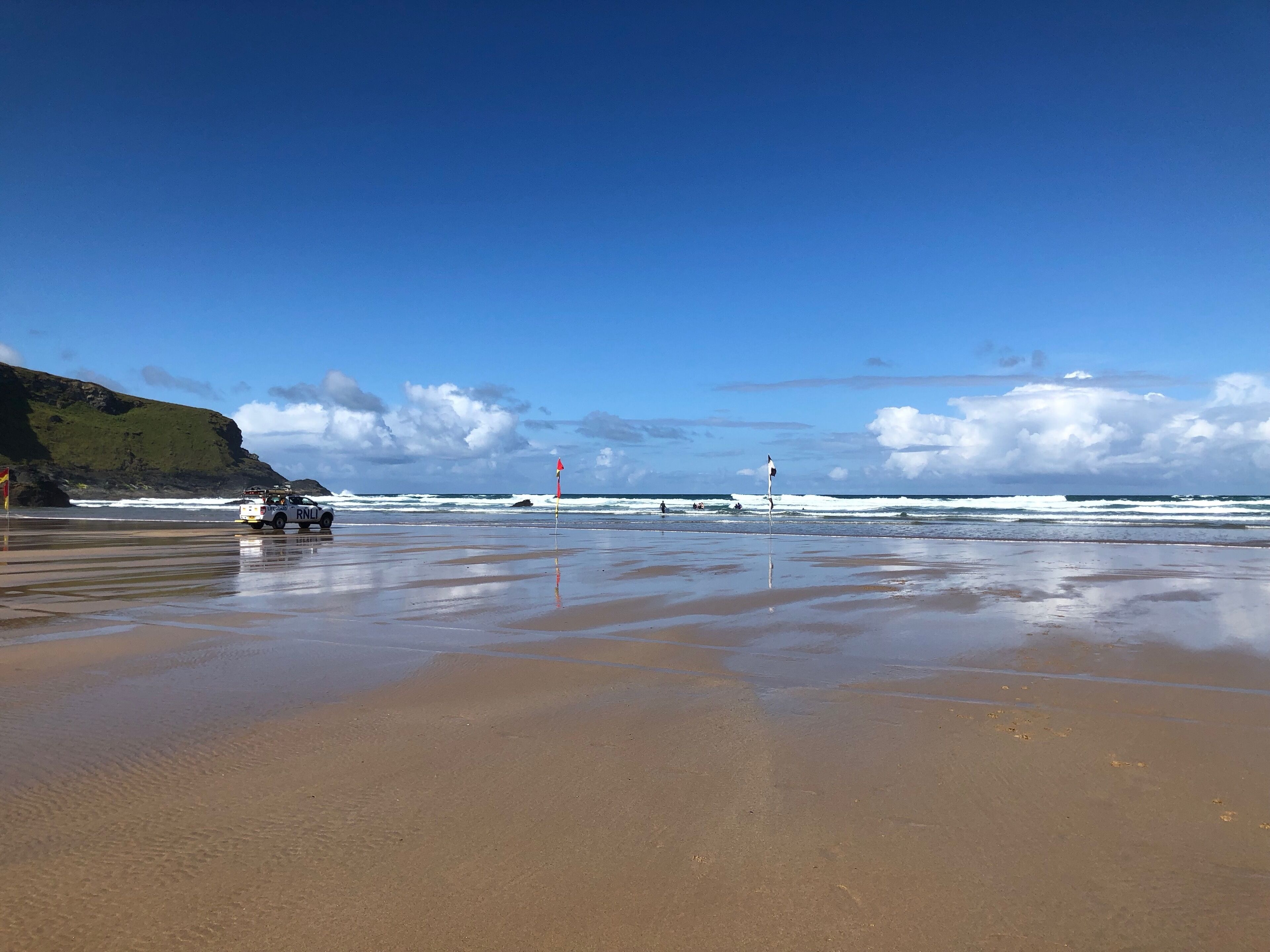 A beach with a lifeguard station, a rocky cliff, and waves crashing onto the shore.
