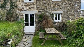 A stone house with a stone pathway leading to a wooden door and a picnic table in the front yard. - Cosy cottage, peaceful setting 5 mins to beautiful sandy beach & fabulous walks! (Mawgan Porth, Cornwall)