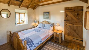 A bedroom with a wooden bed, a window with a view, a wooden door, and a painting on the wall. - Cosy cottage, peaceful setting 5 mins to beautiful sandy beach & fabulous walks! (Mawgan Porth, Cornwall)