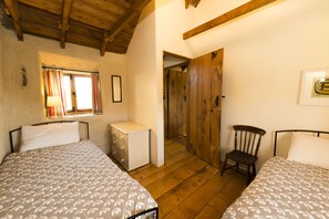 A bedroom with two beds, a wooden chair, a small bedside table, and a window with curtains. - Cosy cottage, peaceful setting 5 mins to beautiful sandy beach & fabulous walks! (Mawgan Porth, Cornwall)