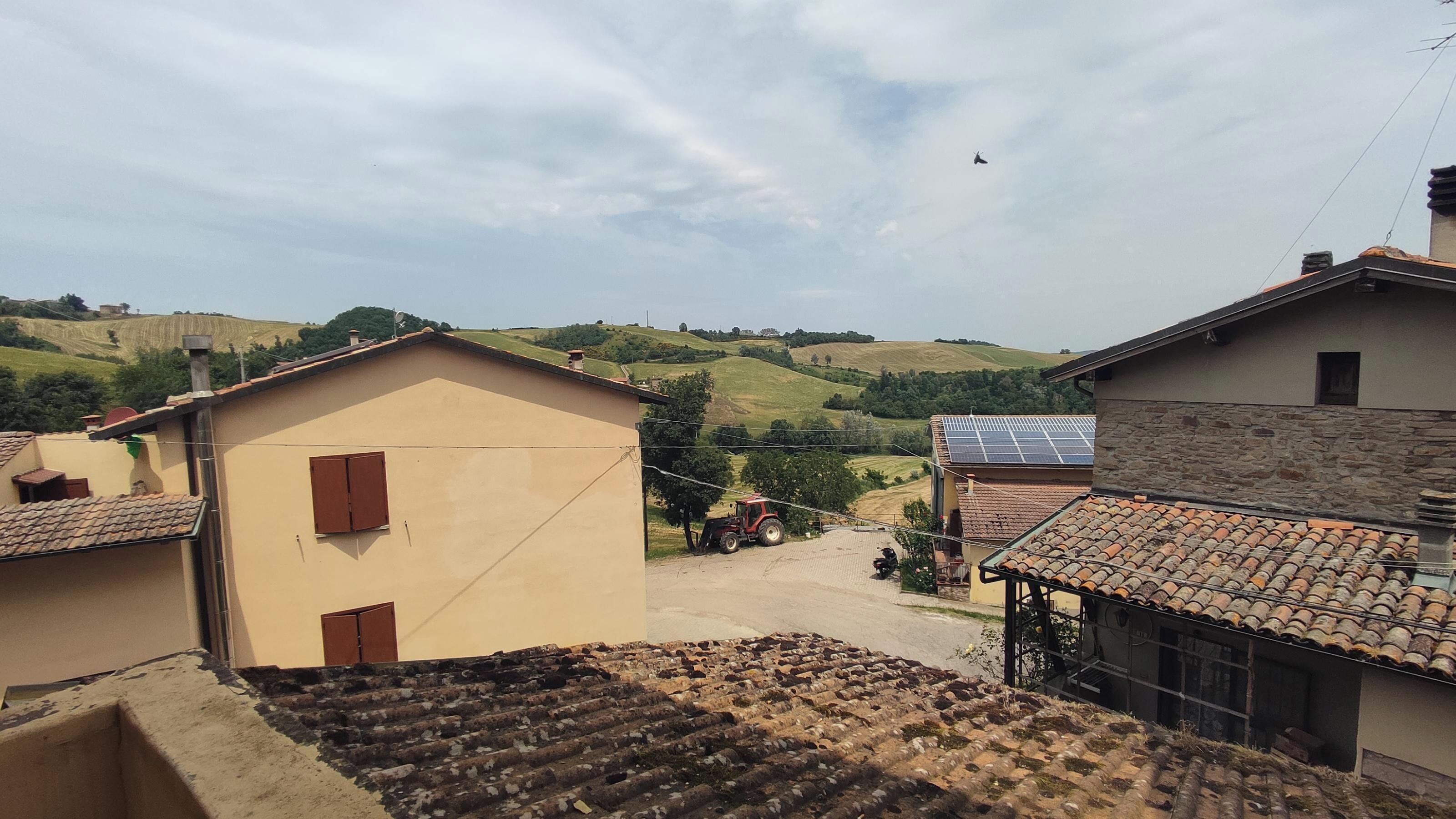 Un pueblo rural con edificios de tejas color terracota, un tractor y paneles solares en una casa.