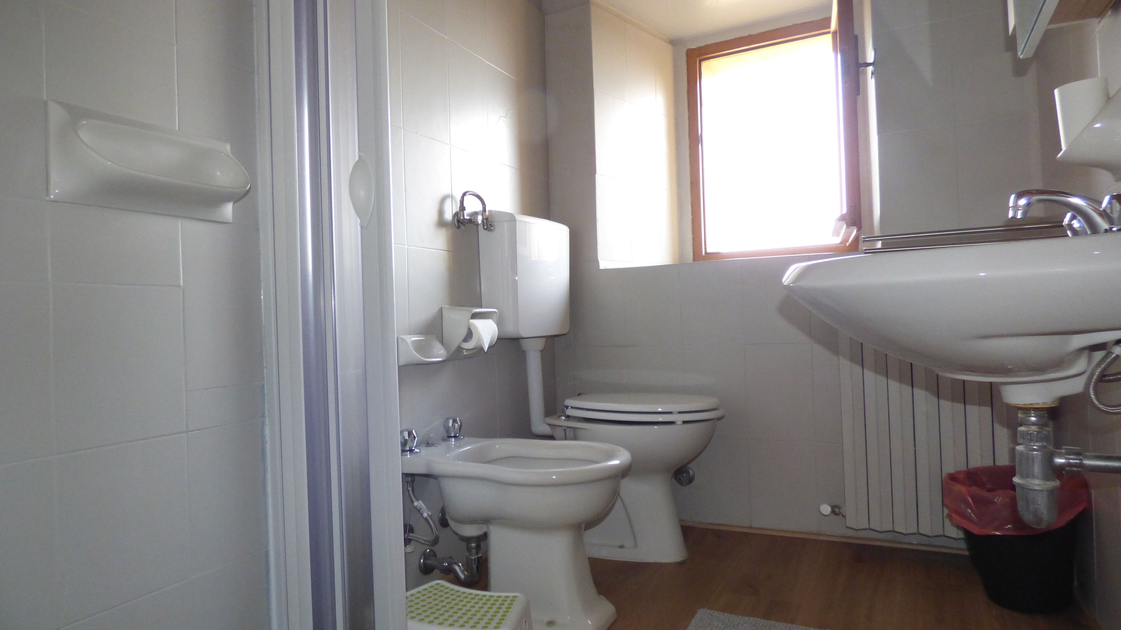 A bathroom with a toilet, bidet, sink, and a window.