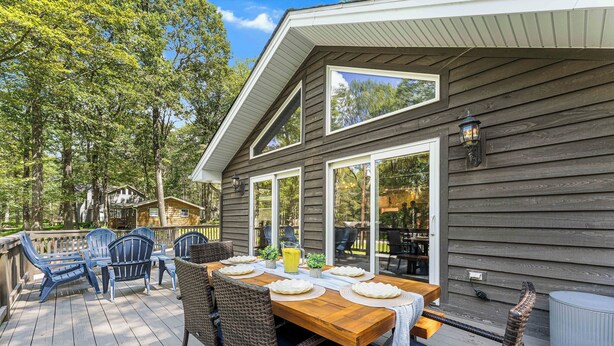 A wooden deck with a dining table set for four, surrounded by wicker chairs. - PBJ Chalet – Modern Pocono Stay w/ Game Room, EV Charger & Fireplaces (Pocono Lake)