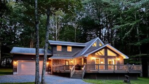 A two-story log cabin with a stone foundation, a covered porch, and a gravel driveway. - PBJ Chalet – Modern Pocono Stay w/ Game Room, EV Charger & Fireplaces (Pocono Lake)