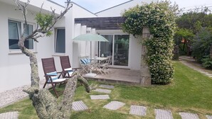 A modern house with a patio area featuring two wooden chairs, a table, and a green umbrella.